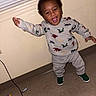 toddler, child, dinosaur_sweater, green_shoes, indoor, floor, window_blinds, joyful, smiling, standing, arms_outstretched, beige_wall, clothing, person, portrait, happy, casual, cute, young_child, playful