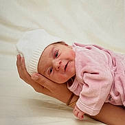 Léonie a rejoint le concours — aidez-le/la à gagner de superbes lots ! baby, newborn, infant, knit_hat, pink_clothing, adult_hand, holding, blanket, bed, portrait, rosy_cheeks, cute, tiny, sleepy, side_view, studio_style, soft_light, newborn_photography, warmth, skin