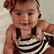 Alaya is registered to the contest to win money with this photo: baby, smiling, headband, gold_bow, striped_outfit, chubby_cheeks, sitting, cute, happy, portrait, infant, child, face, skin, eyes, mouth, arms, legs, white_background, clothing