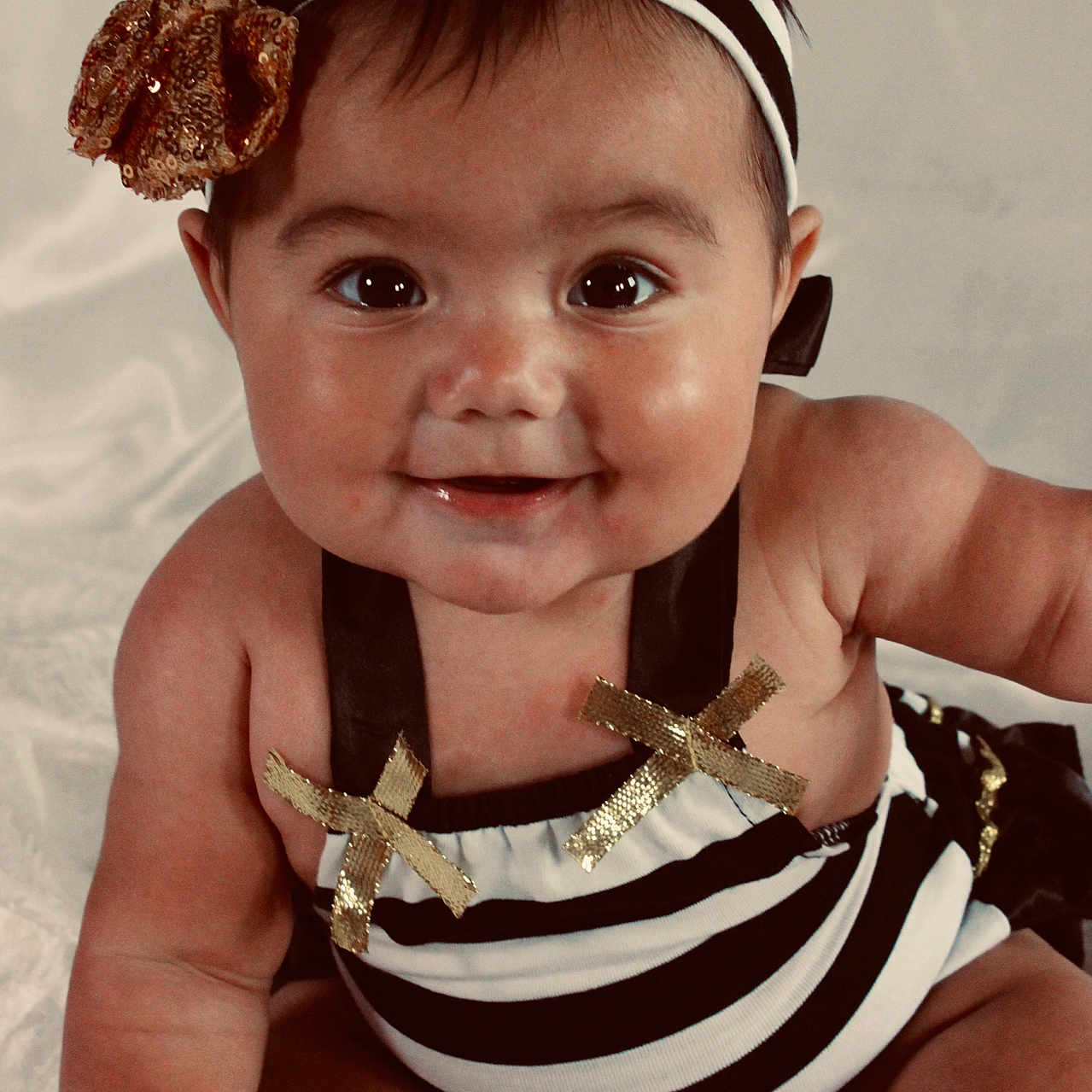 Alaya is registered to the contest to win money with this photo: arms, baby, child, chubby_cheeks, clothing, cute, eyes, face, gold_bow, happy, headband, infant, legs, mouth, portrait, sitting, skin, smiling, striped_outfit, white_background