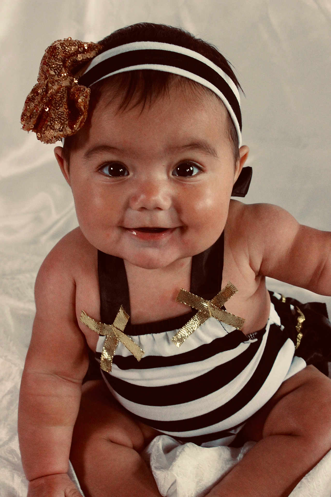 Alaya is registered to the contest to win money with this photo: baby, smiling, headband, gold_bow, striped_outfit, chubby_cheeks, sitting, cute, happy, portrait, infant, child, face, skin, eyes, mouth, arms, legs, white_background, clothing