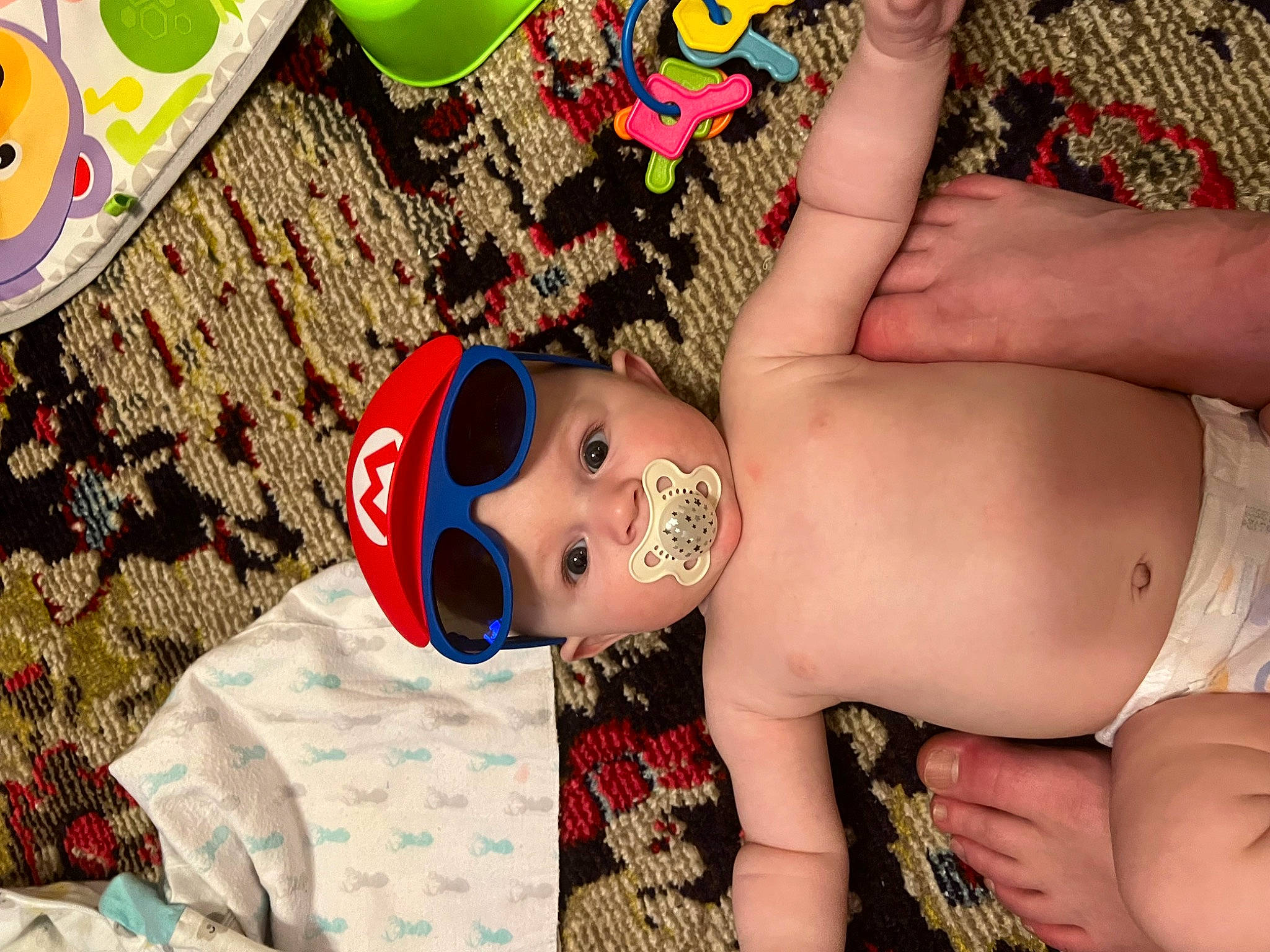 Beau is registered to the contest to win money with this photo: arm, black_hair, chest, eyelash, eyewear, finger, green, hand, happy, headwear, human_body, nail, pattern, person, pink, skin, thigh, toddler, toy, trunk