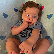 Felipe is registered to the contest to win money with this photo: baby, infant, curly_hair, blue_onesie, blanket, heart_pattern, feet, hand, fingers, lying_down, cute, child, skin, portrait, indoor, soft_texture, colorful, expression, small_person, relaxed