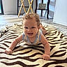arm, baby, child, clothing, crawling, curly_hair, floor, happy, head, home, indoor, person, portrait, rug, shelf, smiling, table, tongue_out, wooden_furniture, zebra_pattern