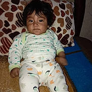 Karla is registered to the contest to win money with this photo: baby, child, pajamas, curly_hair, heart_pattern, pillow, blanket, indoor, cute, portrait, cozy, infant, furniture, resting, patterned_clothing, smiling, person, young_child, seated, home