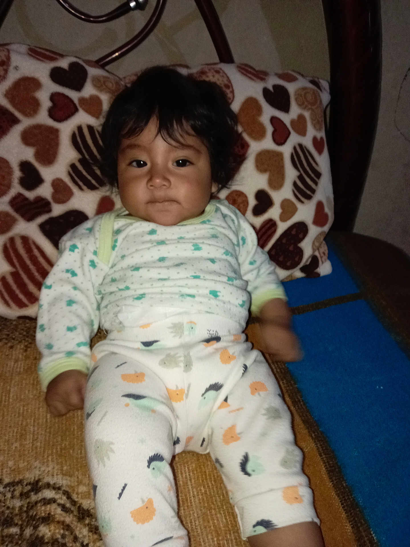 Karla is registered to the contest to win money with this photo: baby, child, pajamas, curly_hair, heart_pattern, pillow, blanket, indoor, cute, portrait, cozy, infant, furniture, resting, patterned_clothing, smiling, person, young_child, seated, home