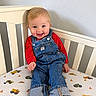 baby, bare_feet, bedsheet, blond_hair, blue_eyes, child, construction_vehicles, crib, denim, furniture, happy, indoor, infant, nursery, overalls, photography, portrait, red_shirt, sitting, smiling
