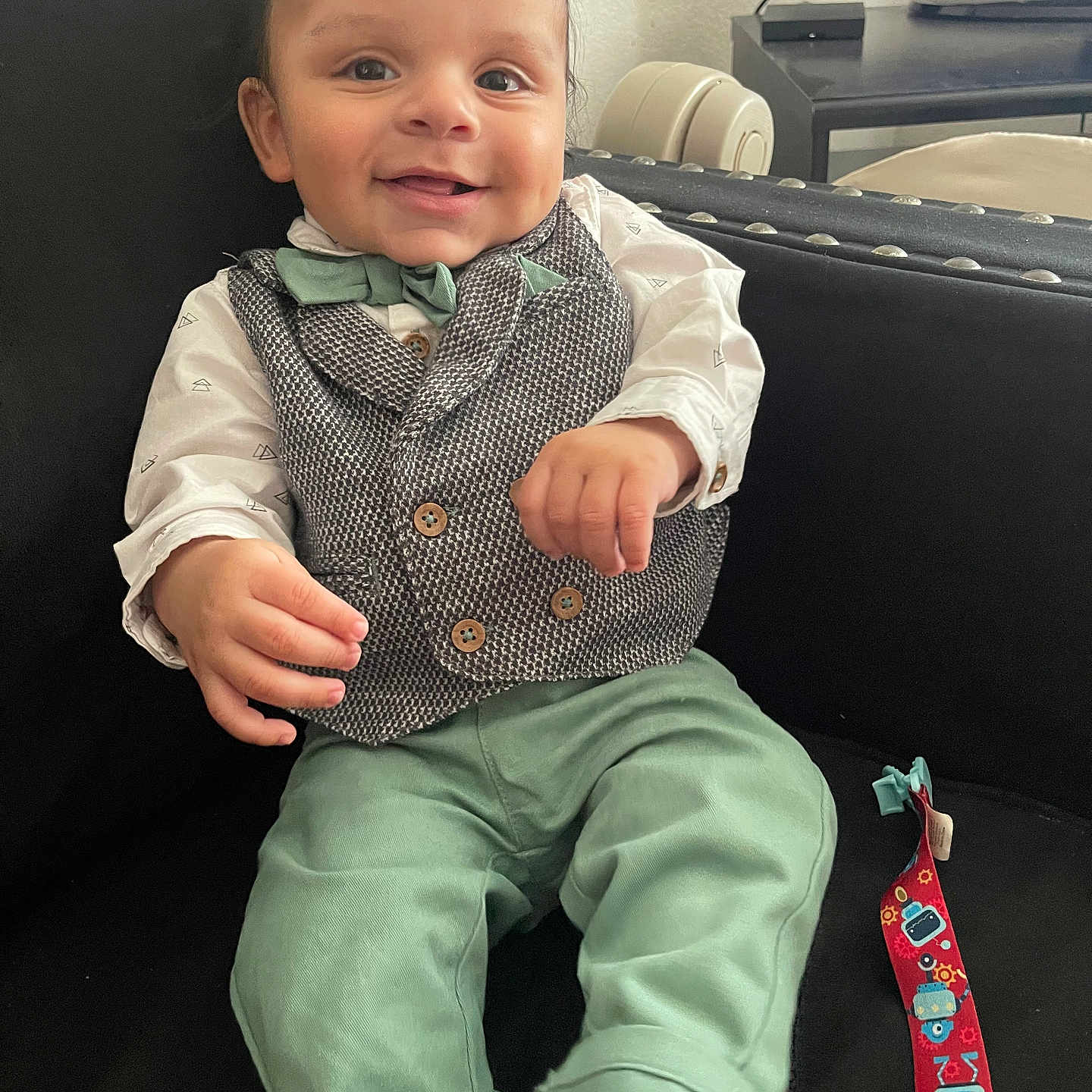 Jayvon joined the competition — help win amazing prizes! baby, child, smiling, sitting, clothing, vest, bow_tie, green_pants, white_shirt, couch, black_couch, toy, colorful_toy, face, happy, indoors, television, furniture, person, portrait