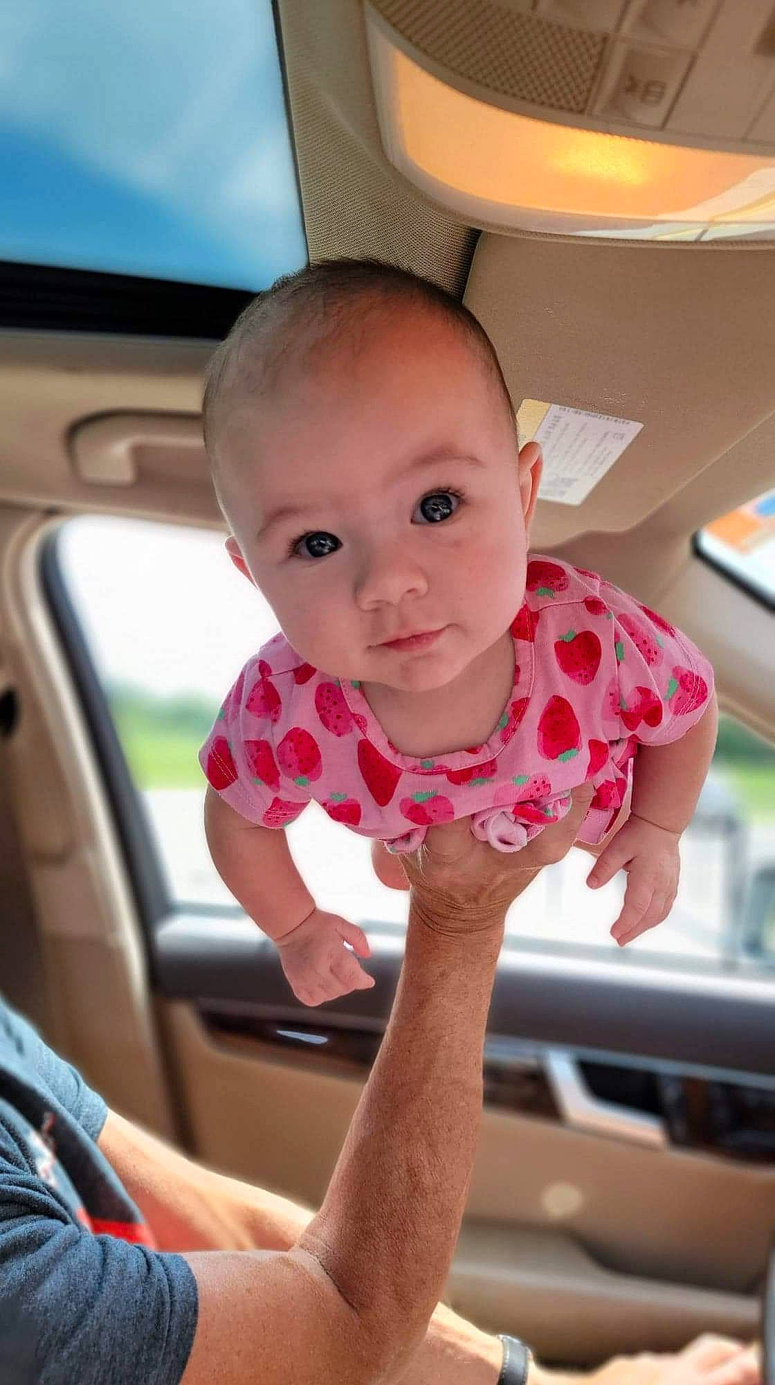 Aylah is registered to the contest to win money with this photo: automotive_exterior, baby, baby_toddler_clothing, car_seat, cheek, child, finger, fun, hand, human_leg, lip, mouth, nail, nose, person, sitting, skin, t_shirt, thumb, toddler