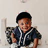 baby, child, baseball, cap, smile, sportswear, blue_clothing, striped_pants, socks, sitting, indoor, toy, soft_lighting, portrait, cute, decorations, tassels, happy, person, infant