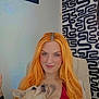 woman, dog, indoor, portrait, red_hair, smile, tattoo, piercing, necklace, chair, wall_art, patterned_wall, pet, small_dog, casual, friendly, looking_up, long_hair, seated, human