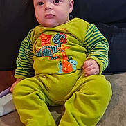 Elyas participe au concours pour gagner de l'argent avec cette photo : baby, infant, child, onesie, green_clothing, dinosaur_design, couch, cushion, indoor, seated, portrait, cute, young_child, face, person, cozy, soft_fabric, home, casual, expression