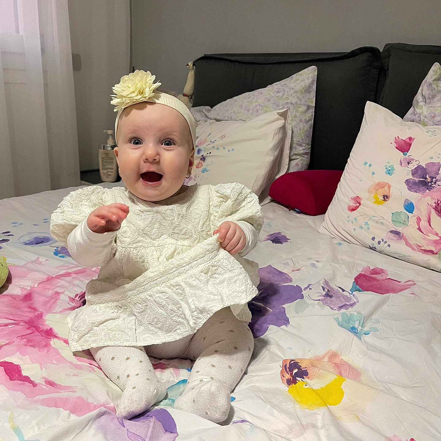 Madina a rejoint le concours — aidez-le/la à gagner de superbes lots ! baby, bed, blanket, child, comfort, cute, decor, floral_bedspread, flower, happy, headband, home, indoors, infant, person, pillow, sitting, smiling, soft_lighting, white_dress