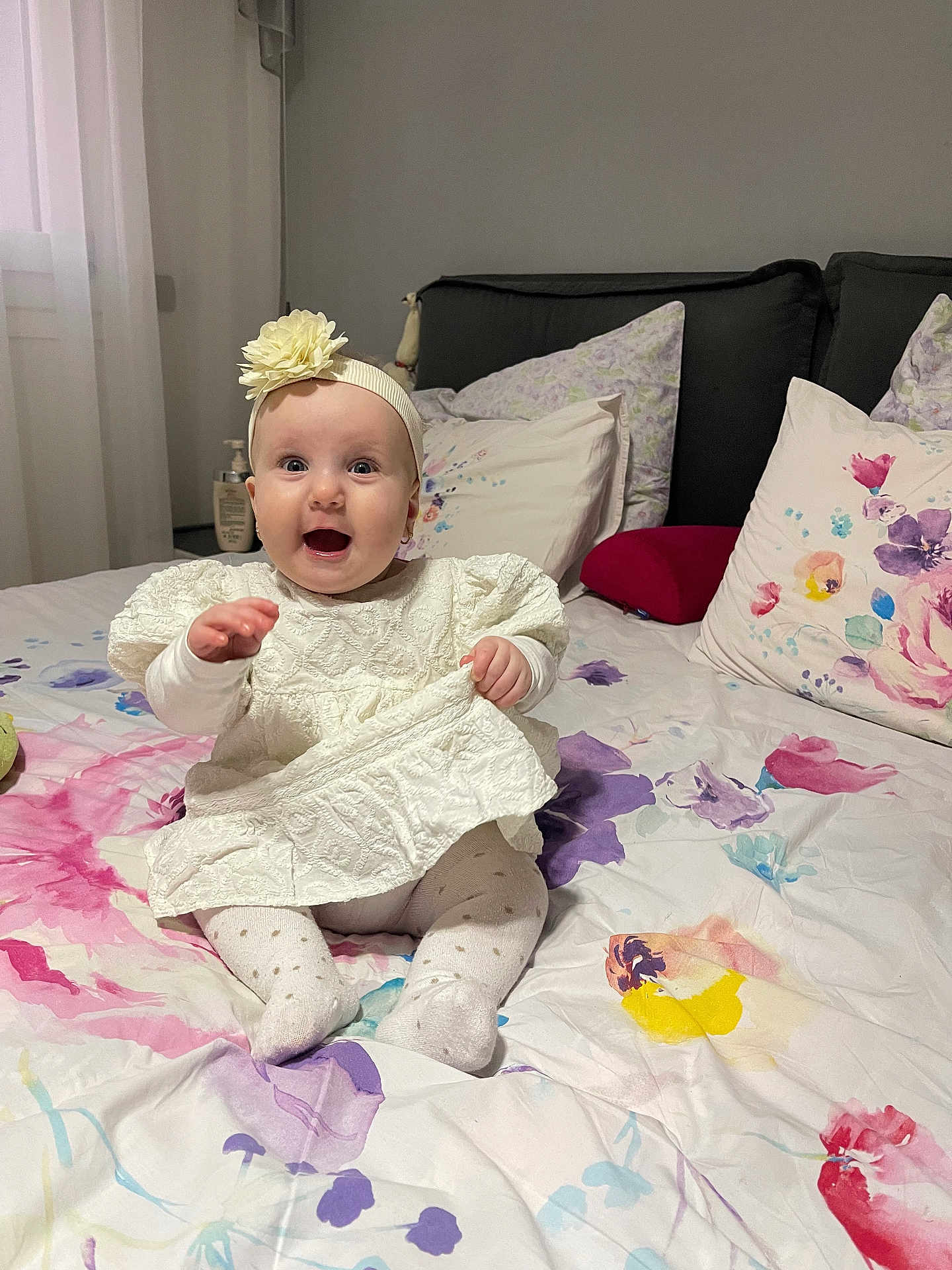Madina a rejoint le concours — aidez-le/la à gagner de superbes lots ! baby, bed, blanket, child, comfort, cute, decor, floral_bedspread, flower, happy, headband, home, indoors, infant, person, pillow, sitting, smiling, soft_lighting, white_dress