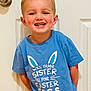 Colt is registered to the contest to win money with this photo: child, boy, smiling, blue_shirt, easter, door, indoor, happy, curly_hair, short_sleeve, playful, standing, casual, light_skin, young, toddler, person, expression, front_view, cute