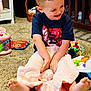 toddler, child, smiling, playing, blanket, stuffed_animal, toy, carpet, indoor, crib, basket, clothing, happy, barefoot, curly_hair, person, room, furniture, floor, baby