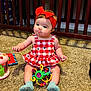Brinley is registered to the contest to win money with this photo: baby, child, girl, red_bow, red_dress, carpet, toy, crib, indoor, playful, sitting, headband, colorful_toy, wooden_crib, blanket, cute, infant, floor, sock, smiling