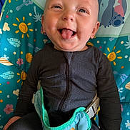 Oliver joined the competition — help win amazing prizes! baby, infant, child, smiling, tongue_out, sitting, portrait, face, eyes, black_clothing, jumpsuit, harness, seat, activity_seat, colorful, patterned_background, stitch, indoor, happy, playful