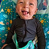 baby, infant, child, smiling, tongue_out, sitting, portrait, face, eyes, black_clothing, jumpsuit, harness, seat, activity_seat, colorful, patterned_background, stitch, indoor, happy, playful
