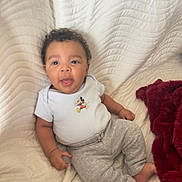 Ethan participe au concours pour gagner de l'argent avec cette photo : baby, blanket, child, curly_hair, cute, grey_pants, happy, indoors, infant, mickey_mouse, onesie, person, portrait, red_blanket, relaxed, sitting, smiling, soft_texture, tongue_out, white_blanket