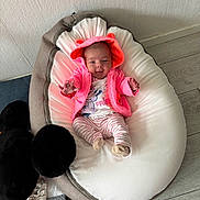 Léonie a rejoint le concours — aidez-le/la à gagner de superbes lots ! baby, infant, pink_hoodie, beanbag, cushion, floor, toy, soft_toy, striped_pants, socks, wall, wood_floor, child, person, indoor, cute, smiling, reaching, comfortable, home