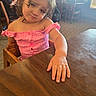 Annalise is registered to the contest to win money with this photo: child, toddler, baby, portrait, restaurant, high_chair, table, pink_outfit, long_hair, brown_hair, face, eyes, smile, sitting, reaching, hand, wooden_furniture, indoor, dining_area, candid