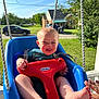 baby, child, swing, blue, red, playful, tongue_out, porch, daylight, outdoor, grass, car, house, trees, smiling, person, seat, rope, sunlight, happy