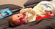 Ethan Zaid is registered to the contest to win money with this photo: baby, blanket, bed, pillow, tablet, screen, child, indoor, soft, cozy, lying, curious, face, eyes, red_clothing, home, technology, resting, infant, sleepy