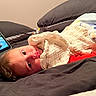 baby, blanket, bed, pillow, tablet, screen, child, indoor, soft, cozy, lying, curious, face, eyes, red_clothing, home, technology, resting, infant, sleepy