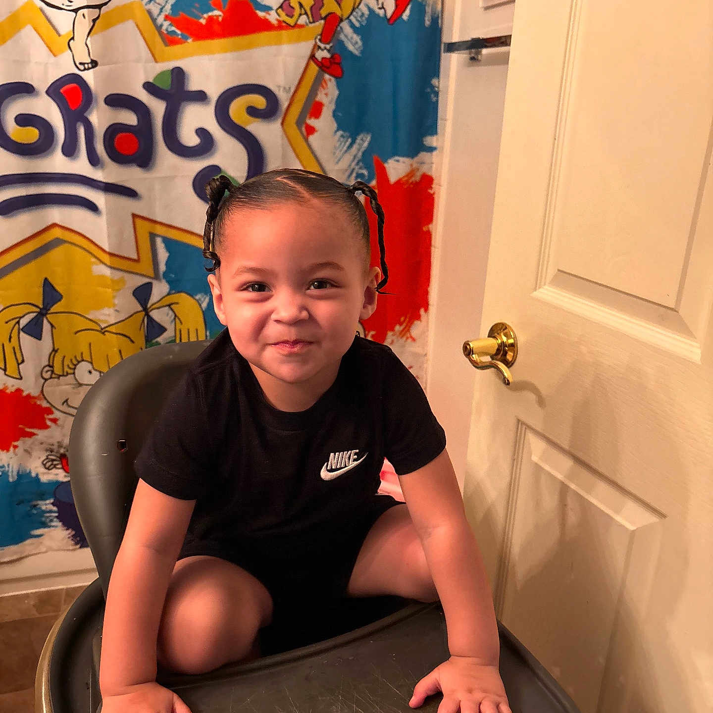 Abria is registered to the contest to win money with this photo: black_clothing, braided_hair, cartoon_characters, child, colorful_curtain, door, face, golden_door_handle, happy, high_chair, home, indoor, mischievous, nike_logo, person, playful, portrait, sitting, smiling, young_child