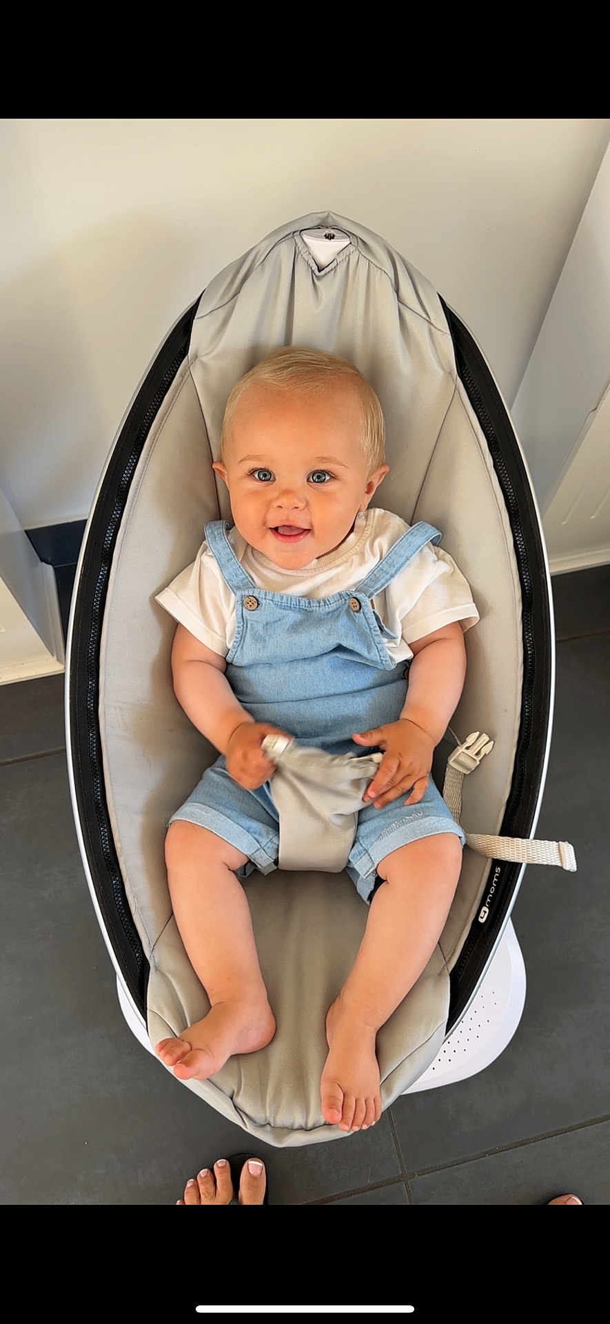 Dario a rejoint le concours — aidez-le/la à gagner de superbes lots ! baby, child, smiling, blue_eyes, denim_overalls, white_tshirt, baby_rocker, safety_strap, cute, happy, indoor, floor_tiles, barefoot, toes, person_feet, light_skin, short_hair, infant, comfortable, seated