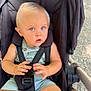 toddler, child, stroller, baby, blue_eyes, blond_hair, outdoor, sunlight, seatbelt, curious, hands, feet, clothing, person, wheels, black_fabric, safety_harness, expression, closeup, portrait