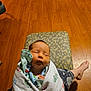 baby, newborn, sleeping, blanket, handprints, infant, wrapped, person, lap, floor, wooden_floor, pajamas, cozy, indoors, relaxing, cute, peaceful, child, human, portrait