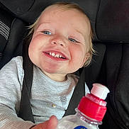 Luka is registered to the contest to win money with this photo: toddler, child, smiling, car_seat, seatbelt, bottle, pop_tops, blue_eyes, messy_face, long_sleeve_shirt, gray_shirt, happy, close_up, indoors, baby, person, portrait, young_child, cute, hands