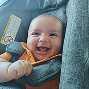 Ezekiel joined the competition — help win amazing prizes! baby, smiling, car_seat, child, orange_shirt, happy, infant, portrait, face, seatbelt, child_safety, cute, indoors, person, skin, hand, young_child, seat, closeup, bright