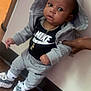 baby, child, hoodie, sweatpants, nike, indoor, flooring, wood_floor, hand_support, socks, knitted_slippers, gold_chain, curious, person, standing, casual_clothing, black_shirt, gray_clothing, wide_eyes, young_child