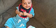 Christopher is registered to the contest to win money with this photo: baby, child, smiling, blue_clothing, bib, couch, brown_couch, blanket, floral_pattern, indoor, happy, infant, person, socks, relaxed, seated, cute, small_blanket, home, casual