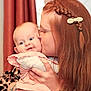 baby, woman, kiss, red_hair, braid, bow, indoor, curtain, pink_clothing, happy, smile, holding, affection, face, person, family, love, closeup, head, candid