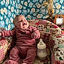 baby, infant, smiling, pink_clothing, bottle, seated, patchwork_chair, teddy_bear_pattern, heart_pattern, indoor, wallpaper, floral_wallpaper, happy, child, cute, cozy, furniture, room, portrait, milk_bottle