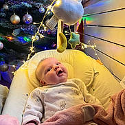 Juliette a rejoint le concours — aidez-le/la à gagner de superbes lots ! baby, blanket, pajamas, mobile, moon, star, fairy_lights, christmas_tree, ornaments, indoor, infant, smiling, face, bed, cozy, holiday, decorations, soft_toys, child, warm