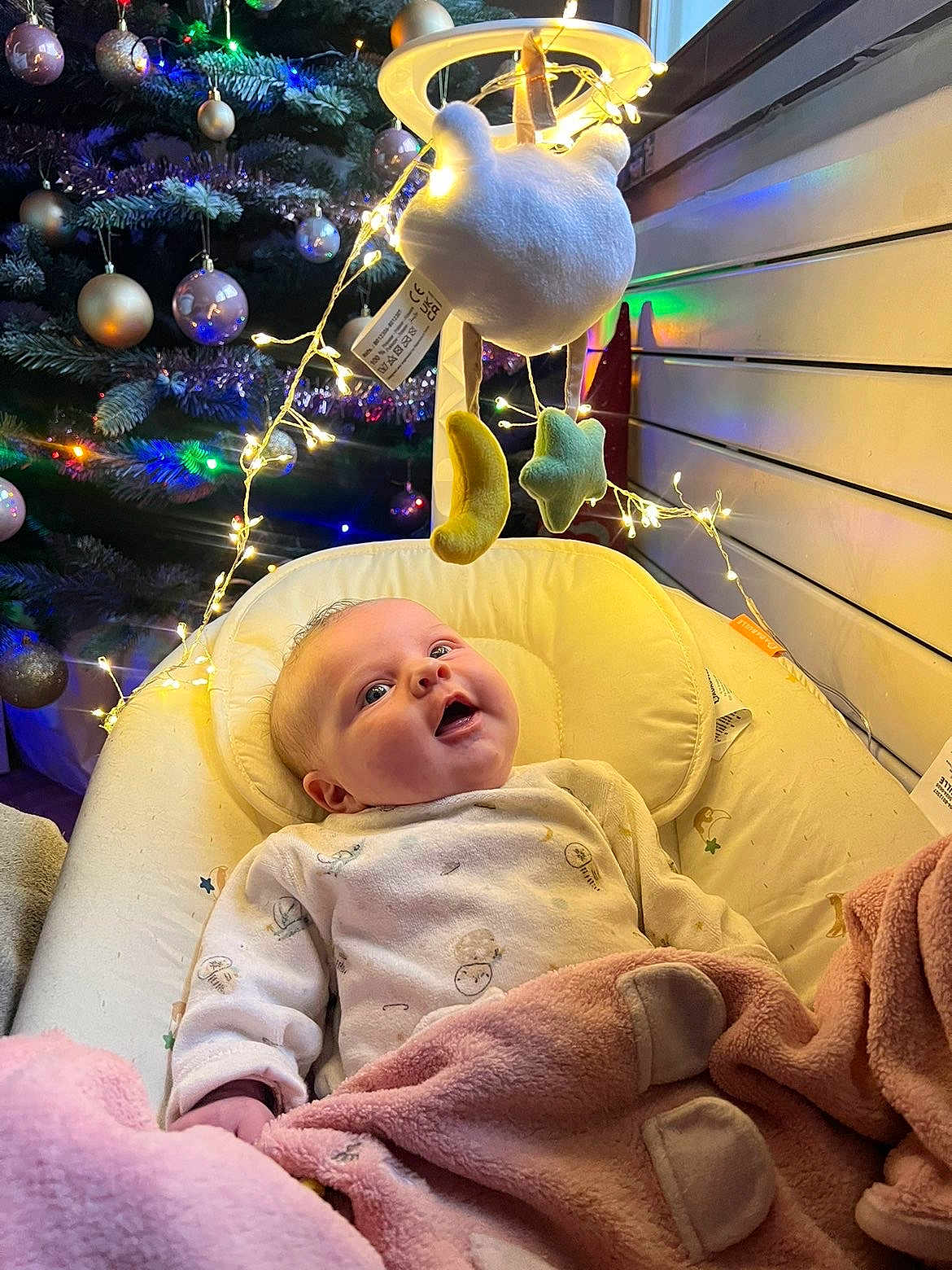 Juliette a rejoint le concours — aidez-le/la à gagner de superbes lots ! baby, blanket, pajamas, mobile, moon, star, fairy_lights, christmas_tree, ornaments, indoor, infant, smiling, face, bed, cozy, holiday, decorations, soft_toys, child, warm