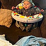 Grayson is registered to the contest to win money with this photo: baby, baby_seat, blanket, brown_couch, cap, child, clothing, colorful, couch, cozy, face, home, indoor, infant, onesie, person, playful, seat, tongue_out, toy