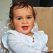 Lya participe au concours pour gagner de l'argent avec cette photo : toddler, child, smiling, face, white_clothing, high_chair, indoors, cute, happy, portrait, baby, infant, person, seated, wooden_buttons, rosy_cheeks, brown_hair, home, furniture, closeup