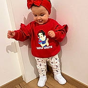 Keyna a rejoint le concours — aidez-le/la à gagner de superbes lots ! toddler, child, red_headband, red_sweater, snow_white, cartoon_print, white_shoes, patterned_pants, wood_floor, corner_wall, indoor, playful, standing, happy, cute, fashion, portrait, person, clothing, headwear