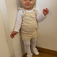 Keyna participe au concours pour gagner de l'argent avec cette photo : toddler, child, indoor, standing, knitted_outfit, headband, flower, white_tights, white_shoes, wooden_floor, wall, smiling, cute, baby, fashion, portrait, person, flooring, footwear, clothing