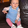 baby, child, girl, blue_dress, pink_tights, white_shoes, bow, earrings, leather_couch, orange_wall, smiling, sitting, indoors, cute, portrait, young_child, fashion, comfortable, bright_eyes, curious