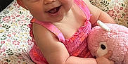 Izzy joined the competition — help win amazing prizes! baby, smiling, pink_outfit, stuffed_animal, floral_cushion, indoor, child, happy, cute, person, soft_toy, patterned_rug, closeup, infant, sitting, cheerful, plush, bright_colors, portrait, adorable
