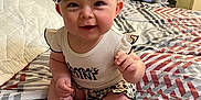 Izzy is registered to the contest to win money with this photo: baby, bed, bedding, bow, child, clothing, cute, foot, hand, happy, headband, indoors, infant, patterned, person, room, sitting, skin, smiling, text_on_clothing