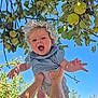 baby, child, smiling, happy, outdoors, apple_tree, fruit, green_apples, blue_sky, sunlight, nature, hands, playful, bonnet, clothing, person, arms, joy, summer, garden