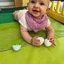 baby, child, play_mat, purple_bib, white_eggs, indoor, smiling, playpen, toy, person, crawling, floor, cute, infant, happy, young_child, colorful, plastic, hand, head